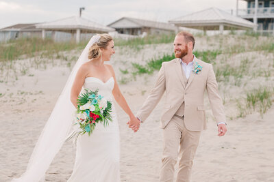 A smiling couple walking the beach during their destination wedding at sunset while enjoying their destination wedding photography session by JoLynn Photography