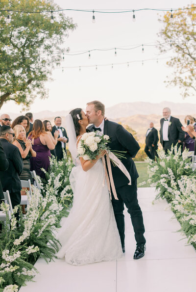 The bride holds a large white rose bouquet as she kisses the groom at Spanish Hills Camarillo, California.