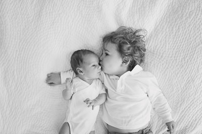 Black and white photograph of newborn baby boy being kissed by older brother