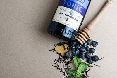 Flat lay of Wild Tonic bottle with blue berries  and tea scattered about