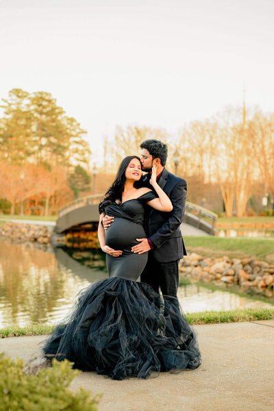 charlotte maternity photo of couple embracing at a charlotte garden.  mom to be is dressed in black dress and father to be is also dressed in black