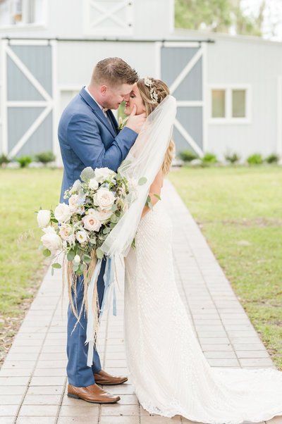 Groom kisses his bride as veil blows in wind and she holds bouquet