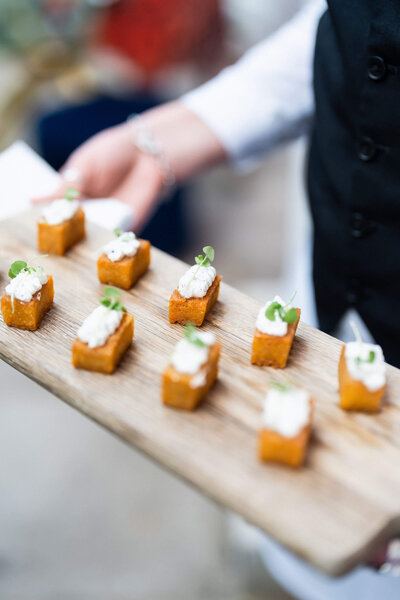 closeup of a wooden tray of canapés presented by a caterer at a luxury party