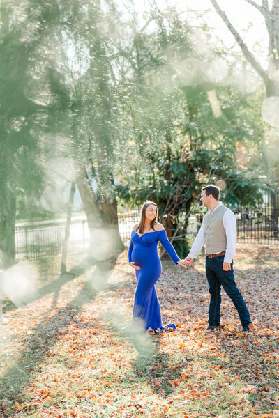 pregnant woman in blue gown walks through garden with husband