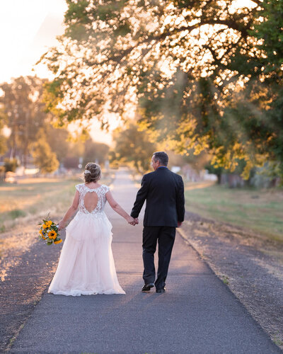 Bride and groom, holding hands, walking away into the sunset