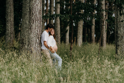 A couple leaning against a tree in a pine tree forest being photographed by maternity photographer tashina narelle photography