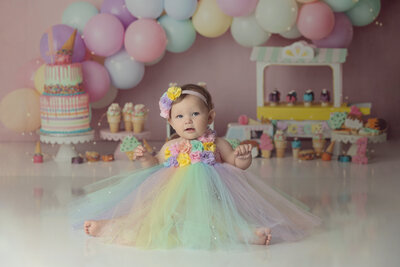 1st Birthday girl wearing a pastel rainbow dress with matching headband with a sweet treat background theme.