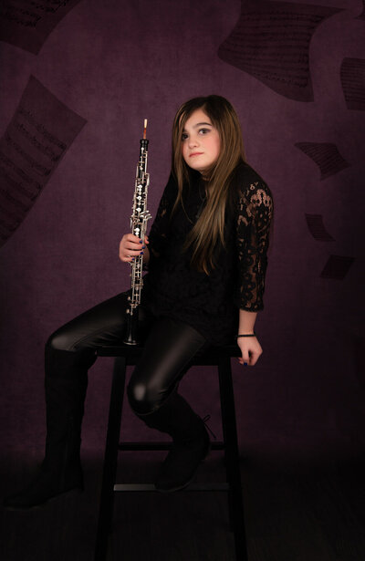 girl-in-black-holding-clarinet-against-purple-backdrop-in-arlington-tx-and-sheet-music-flying