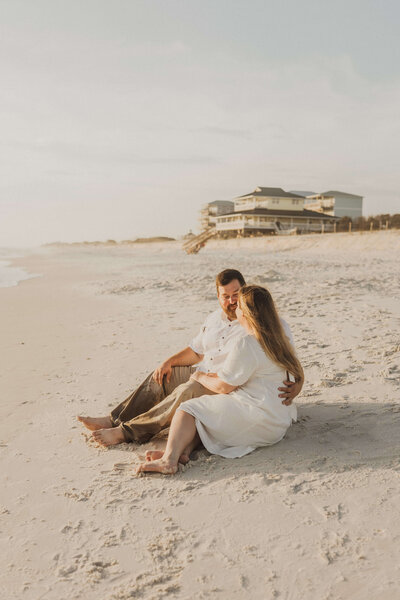 Young newly engaged couple sit side by side on beach in Cape San Blas, Florida