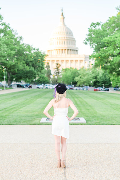 Grad stands in front of the US Capitol while wearing doctoral grad cap during grad session photographed by Cait Kramer