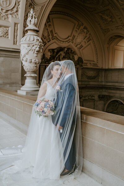 bride and groom standing under veil for portrait in san francisco city hall