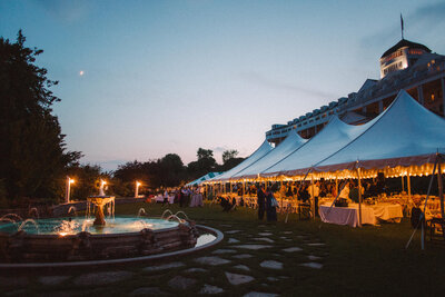 a night image of a tented wedding reception with the moon lit and string lights lit and a water fountain