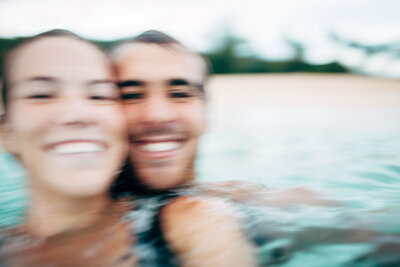 a husband and wife laugh as they get rocked by some waves and the camera creates motion blur