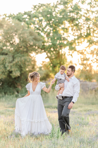 A family walks in a field of poppy flowers, the mother dressed in a long white gown holding her toddler sons hand photographed by Bay area photographer, Light Livin Photography.