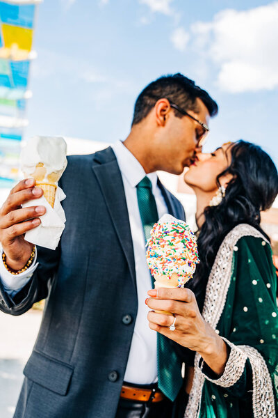 During their unique engagement photography session, an Indian couple kiss holding ice cream cones on a hot day during the summer in Cincinnati, Ohio.