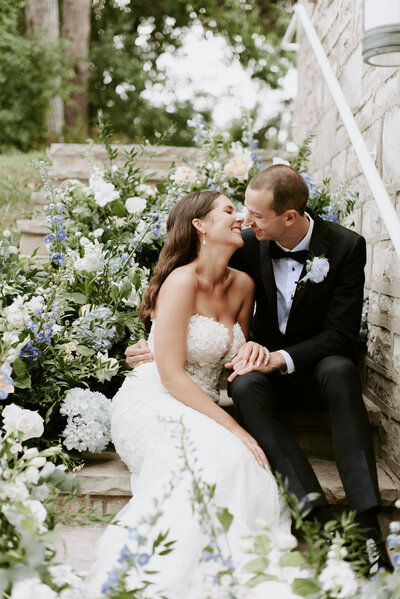 bride and groom sitting on steps surrounded by luxury floral display