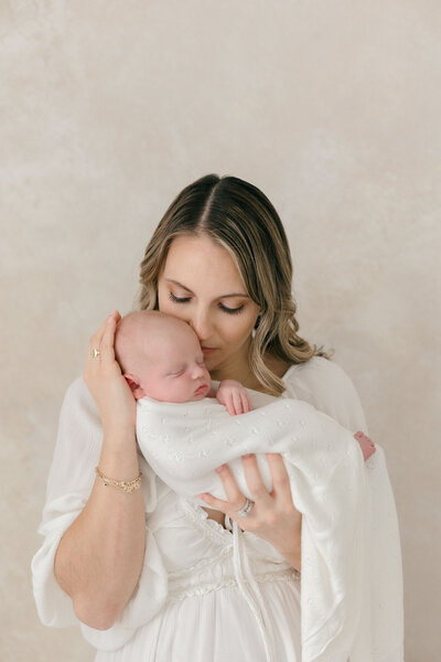 A mom holding her newborn baby close to her face with her eyes closed by NJ Photographer
