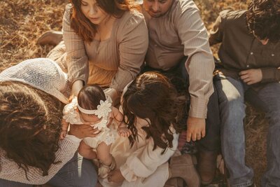 The arrival of your newest family member with our heartwarming outdoors newborn session. The entire family gathers in the grass, captivated by the sweet newborn girl. The oldest boy cradles the baby, creating a touching scene of sibling connection. Dressed in coordinated outfits with warm tones of brown, orange, and beige, this big family radiates love and unity against the natural backdrop.