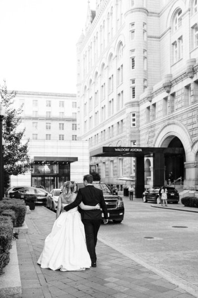 Bride and groom walking hand in hand near the entrance of the Waldorf Astoria Hotel, captured by a luxury wedding photographer.