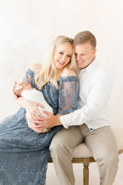 A mother and father cuddling on a bench in front of blush hand-painted canvas by dc newborn photographer