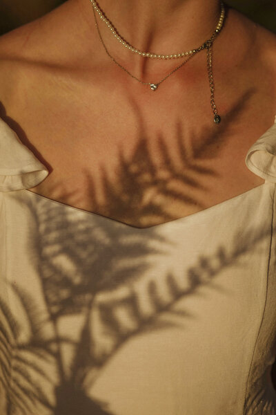 Woman wearing gold necklace with fern shadow and healing crystals nearby