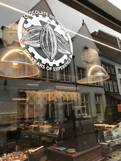 Photograph of chocolate shop window in Bruges with logo on the window.