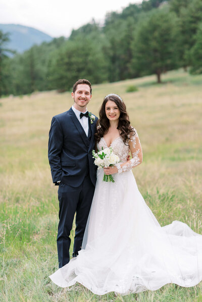 Beautiful bride in white flowing gown stands with fiance and smiles at the camera