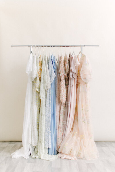 A photo of 7-10 light and neutral colored  dresses hanging on a rack