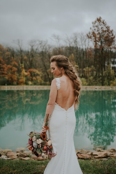 A bride with a thick boho braid standing by a green lake.