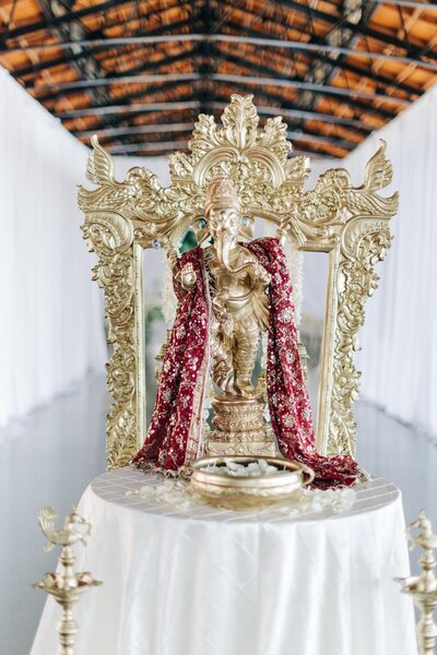 Elegant lord ganesha idol adorned with red flowers, displayed on a white pedestal and ceremonial backdrop.