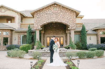 Elegant embrace at Superstition Manor: Groom sidewise, bride with a graceful tilt, holding bouquet, capturing timeless romance in stunning photography
