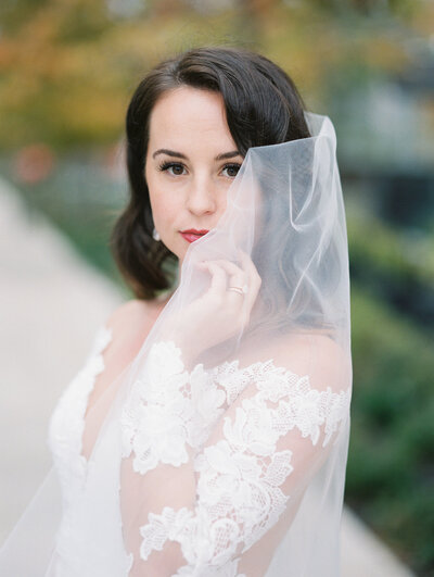 A bride looking at the camera with her hand on her face and her veil covering part of her face
