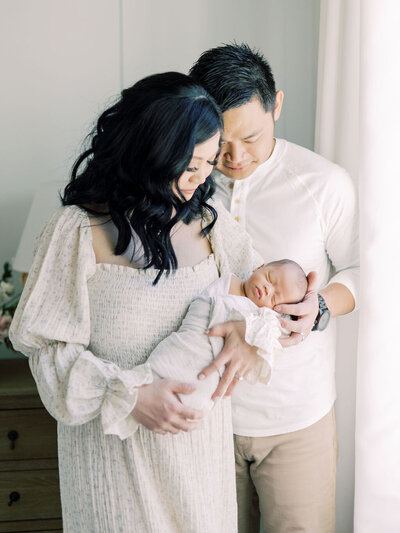 Couple snuggle on bed and cradle baby during newborn session.