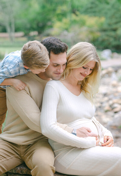 Family of 3 looking down at Mom's pregnant stomach
