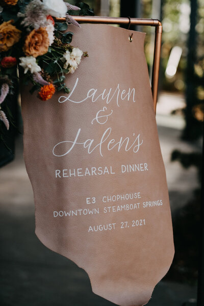Hand painted leather wedding welcome sign with calligraphy hanging on a copper stand, decorated with florals