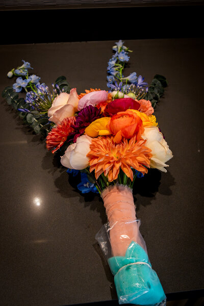 Colorful bridal bouquet with orange, coral, and pink flowers tied with teal ribbon – photographed by wedding photographer Niko Coric – Lumen Clarity Media