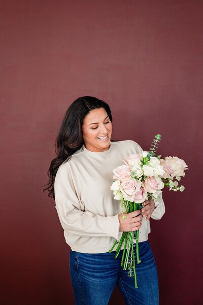Florist holding flowers smiling in front of a maroon wall