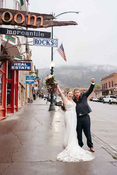 Couple stands on the street in Ouray, Colorado with their arms in the air celebrating their wedding day