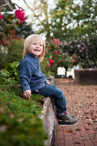 Smiling boy sitting on wooden wall smiling with flowers in the background -Family Photographer Nashville