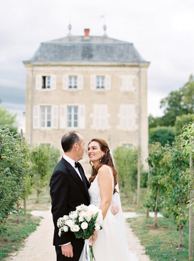 Bride and groom embrace and stare lovingly at each other in front of chateau venue on their wedding day