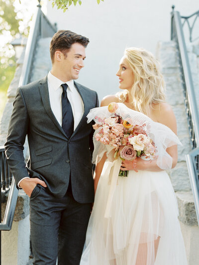 Stylish bride and groom descend stairs while smiling at one another