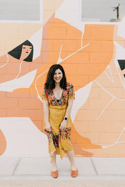 Amber wearing yellow skirt and floral top in front or orange abstract art, Austin branding, family and wedding photographer