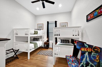 Bedroom with two sets of bunk beds and arcade machine in this three-bedroom, two-bathroom home with fully stocked kitchen, large backyard, grill, and basketball hoop in downtown Waco, TX.
