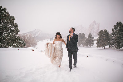 Bride and groom running through the snow at winter wedding in Colorado
