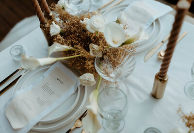Wedding table set with tan menu card on a plate and brown and white flower centerpiece