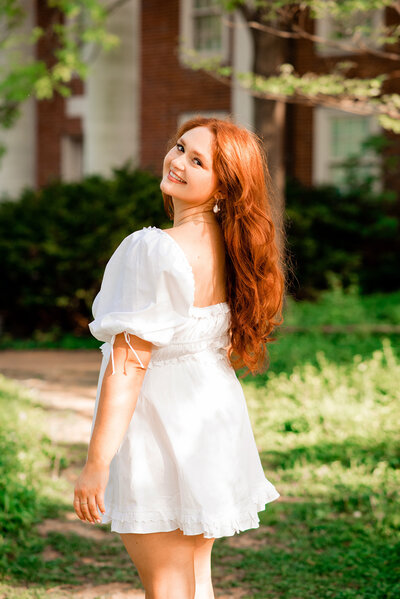 College senior wearing a white dress and smiling over her shoulder at the camera