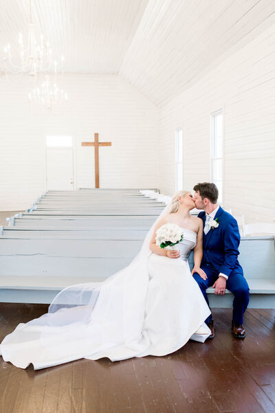 groom in black suit and bride in white gown look at one another in a green field