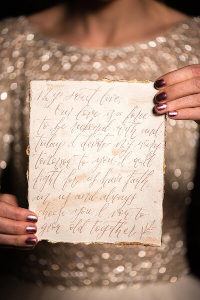 bride holding calligraphy wedding vows on parchment paper wearing gold sequin dress