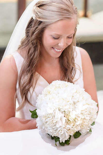 Bride in wedding dress and veil holding white hydrangea bouquet looking down standing in a doorway