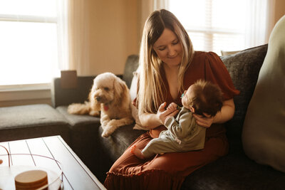 mom smiling at newborn with little white dog in the background